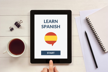 Online learn spanish concept on tablet screen with office objects. All screen content is designed...
