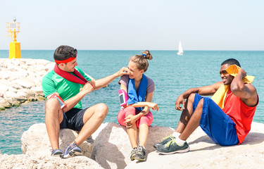 Multiracial friends relaxing after fitness on the beach - Multicultural young teens sitting at  pier rocks with ocean background in hot summer training day - Concept of friendship and healthy life