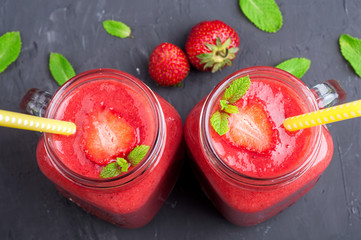 Strawberry smoothies in glass jar, berries and mint on stone background closeup. Healthy food concept