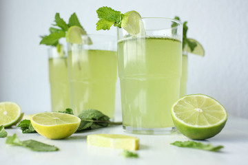 Fresh home-made lemonade with lemon, lime and mint in a glass on white background and ingredients laying on the table