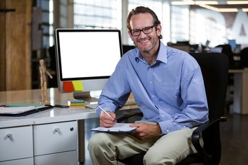 Confident businessman writing on clipboard by desk