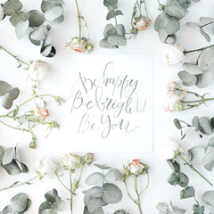 inspirational quote be happy, be bright, be you written in calligraphy style on paper with pink roses and eucalyptus branches on white background. flat lay, top view
