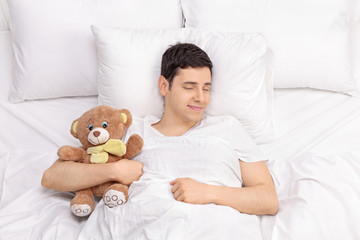 Joyful guy sleeping with a teddy bear