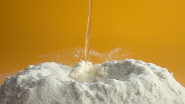 Egg dropping into flour on yellow background, slow motion