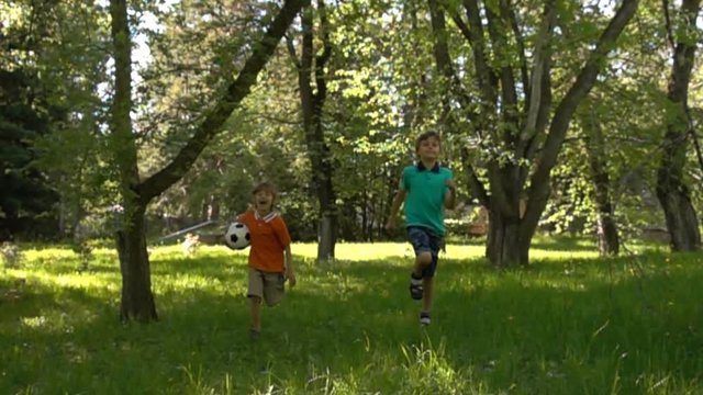 two boys with soccer ball running on grass and smiling, happy kids playing outdoors, summer fun