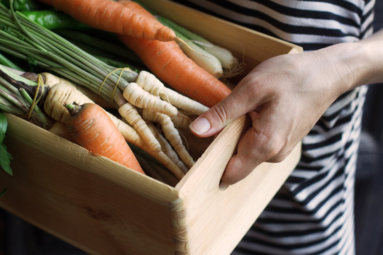 Woman Holding A Wooden Crate Full Of Vegetables At The Market