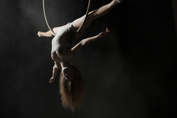 Acrobatic woman doing gymnastic cross twine on aerial hoop