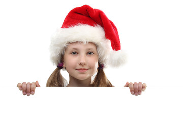 the portrait of smiling little girl on Santa Claus hat peeking by the white board looking at camera isolated on white background.
