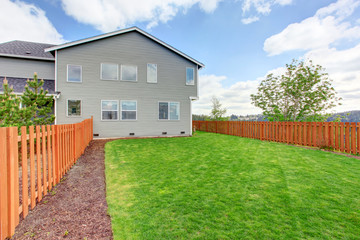 Spacious fenced back yard with green grass. House exterior of a large house.