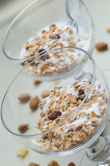 Granola with yoghurt, nuts and fruits in glass bowl on light background. Delicious, healthy sweet dessert for breakfast. Cereal, muesli.  Copy space, closeup.
