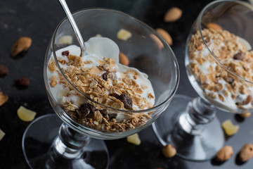 Granola with yoghurt, nuts and fruits in glass bowl on dark background. Delicious, healthy sweet dessert for breakfast. Cereal, muesli.  Copy space, closeup.
