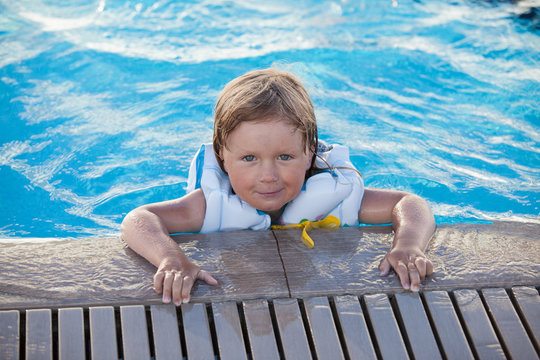 Cute little child swimming with life jacket in outdoor pool
