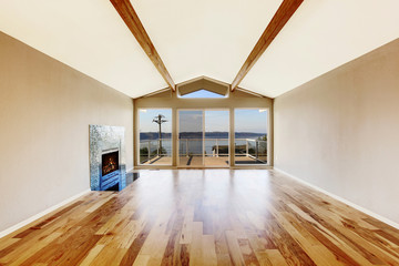 Empty room interior with hardwood floor, vaulted ceiling and fireplace
