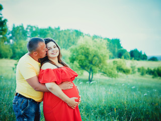 Pregnant woman and her husband with hands on belly outdoors