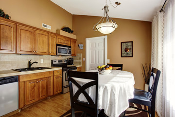 Cozy kitchen and dining room interior with black table set and brown cabinets.