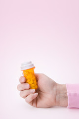Drugs and Pills – A hand holding a bottle of pills. On a pink background.