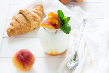 Yogurt with peach in a glass jar on white wooden background. Selective focus