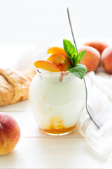 Yogurt with peach in a glass jar on white wooden background. Selective focus