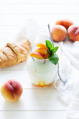 Yogurt with peach in a glass jar on white wooden background. Selective focus