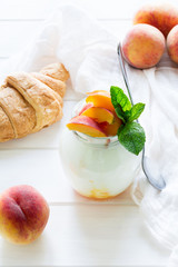 Yogurt with peach in a glass jar on white wooden background. Selective focus