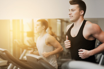 Fototapeta na wymiar smiling men exercising on treadmill in gym