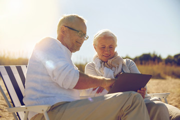 happy senior couple with tablet pc on summer beach