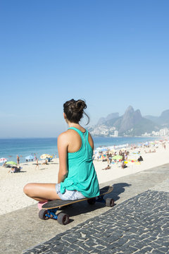 Young carioca Brazilian woman sitting on her skateboard overlooking Ipanema Beach at Arpoador in Rio de Janeiro, Brazil
