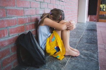 Sad schoolkid sitting alone in corridor