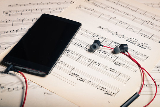 pictured black phone with headphones placed over sheets music.