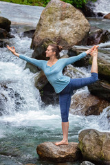 Woman doing yoga asana Natarajasana outdoors at waterfall