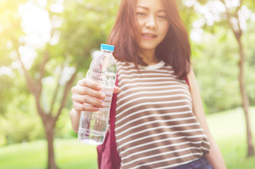 Close up female hand holding water while smiling at summer green park outdoor and bokeh nature background, healthy concept.