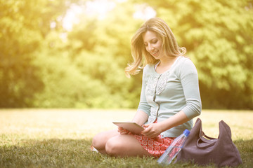 Young woman sitting in a park and surfing Internet over digital tablet