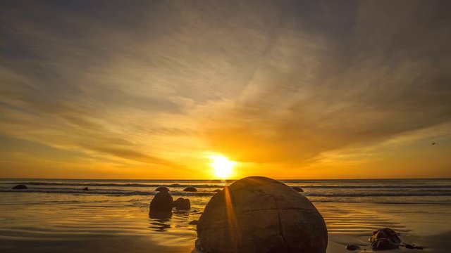 Vibrant Sunrise At Moeraki Boulders- Timelapse. Moeraki Boulders are a group of large spherical stones that have been exposed through shoreline erosion on Koekohe Beach near Moeraki