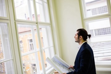 Interior designer holding blueprint while looking through window