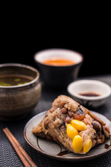 Zongzi or Asian Chinese sticky rice dumplings with Yellow tea, soup, sauce and chopsticks on dark table surface. Zongzi is a traditional Chinese food eaten during the dragon boat festival.