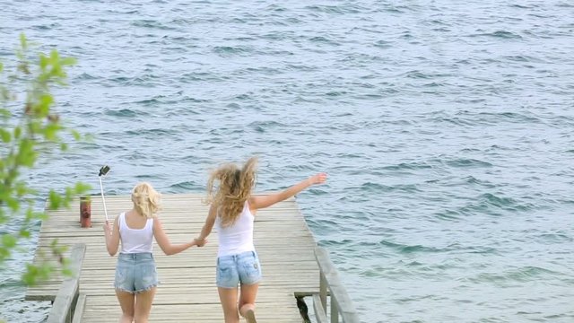 Two friends women taking selfie with mobile phone near the river. Two young girls enjoying near river and taking selfie using smart phone.