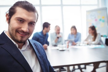 Portrait of smiling businessman against coworkers