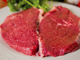 Two piece of raw beef on a plate.