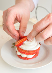 Руки кондитера украшают десерт кусочками клубники