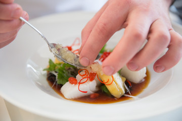 Руки повара украшают блюдо из рыбы белой икрой