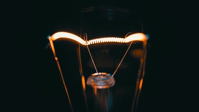 The filament incandescent lamp is lighting and moves on a black background
