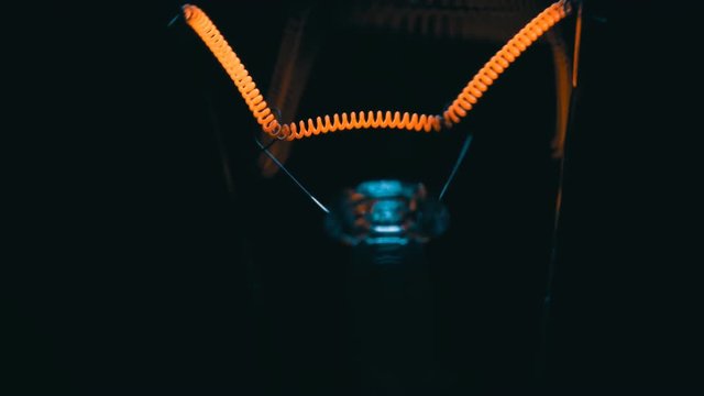 The filament incandescent lamp is lighting and moves on a black background
