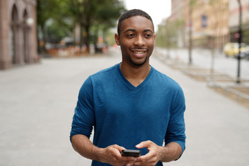 Young black man in city walking texting cell phone