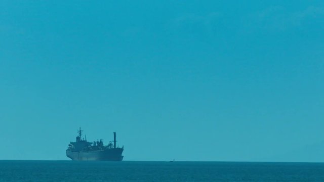 Enormous commercial tanker ship moving slowly across the distant horizon under a clear, blue sky.
