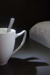 white coffee cup and shadow on the table near the bed