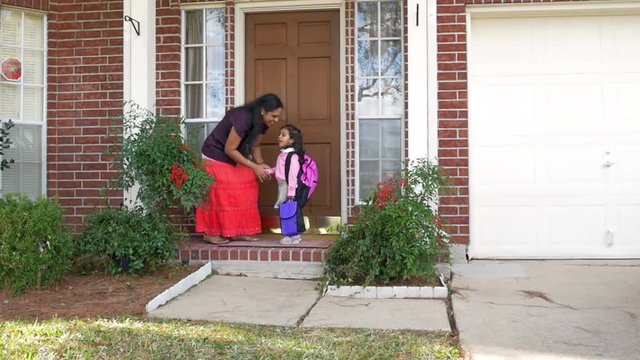 A little girl wearing a backpack gets a little kiss from her mother and a cheerful send off to school.