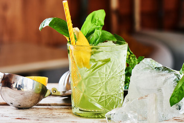 Alcoholic cocktail Basil smash in a glass beaker and a piece of ice on a wooden table