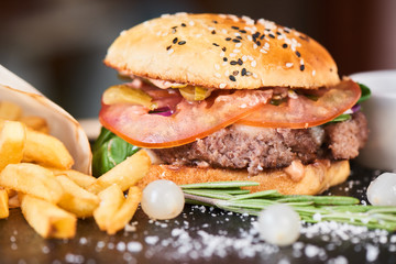 A hamburger consisting of meat patties, cheese and vegetables served on a stone Board closeup