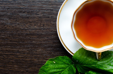 natural herbal antipyretic -organic raspberry leaves tea

in a white porcelain сup with fresh green leaves on a dark wooden table, shot at an angle of 90 degrees, for labels, packages, menus, etc
