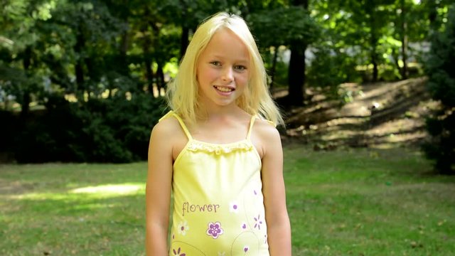 little happy girl stands in the park and smiles - eye contact
